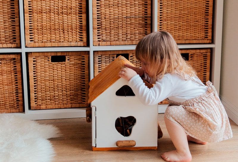 Fotografía de una niña recogiendo sus juguetes en una casita de madera